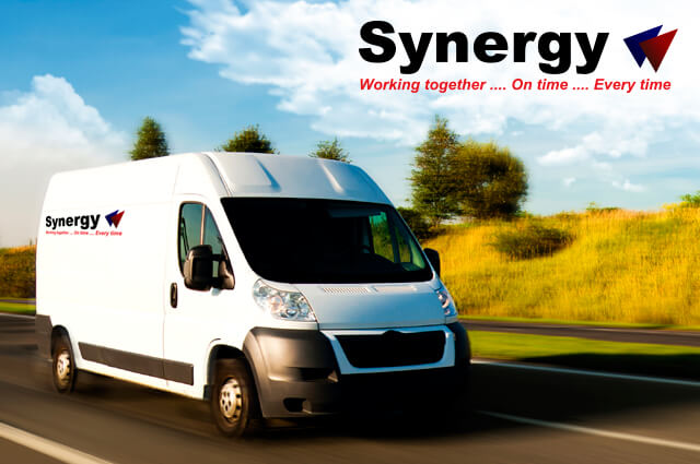 A white delivery van driving on a road with the Synergy Courier Services logo in the right hand corner.